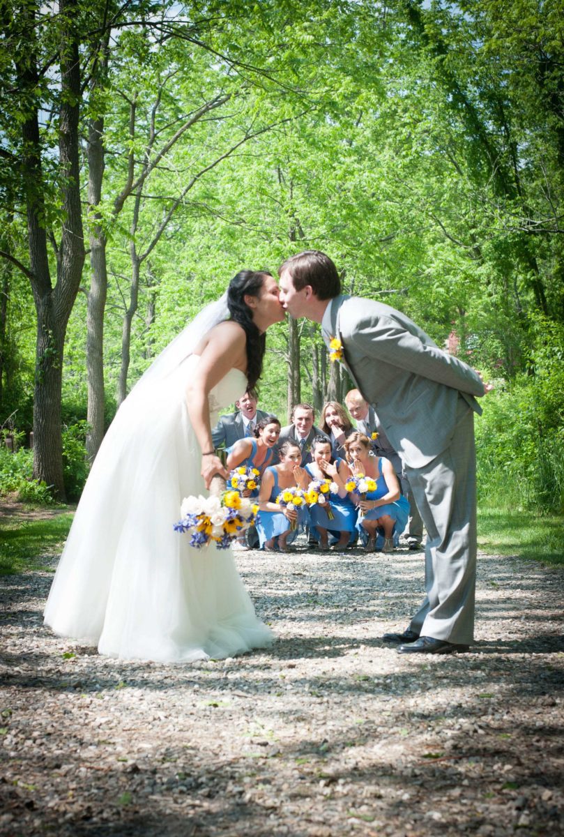 couple kissing while bridal party looks on
