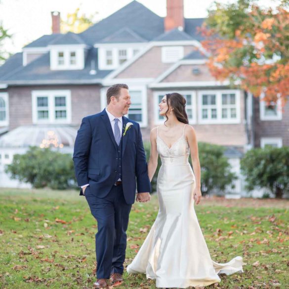 bride-groom-hand-in-hand-across-lawn-with-mansion-in-background